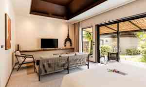 Hotellihuone, jossa moderni sisustus, istuinryhmä, televisio sekä suuret lasiovet, jotka johtavat vehreälle terassille. (Tekoälyn luoma teksti)