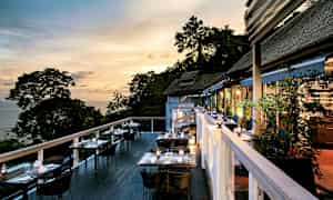 Ulkoterassi, jossa pöytiä ja tuoleja iltahämärässä, näkymä merelle ja puihin. (Tekoälyn luoma teksti)