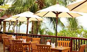 Ulkopöytäryhmiä, joissa puiset tuolit ja pöydät varjoineen, palmuja ympärillä. (Tekoälyn luoma teksti)