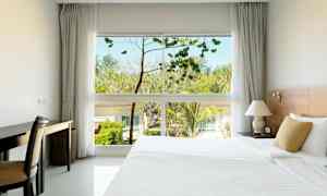 Hotellihuone, jossa on suuri sänky, työpöytä ja ikkuna, josta näkyy puita ja rakennuksia ulkona. (Tekoälyn luoma teksti)