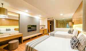 Hotellihuone, jossa kaksi vuodetta, seinään kiinnitetty TV ja lasi-ikkuna kylpyhuoneeseen päin. (Tekoälyn luoma teksti)