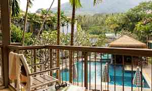 Näkymä parvekkeelta altaalle, jota ympäröivät palmut ja vehreät kasvit, etualalla tuoli ja pöytä. (Tekoälyn luoma teksti)