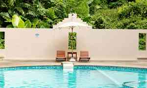 Uima-allas, jossa kaksi aurinkotuolia ja varjo seinän edessä, taustalla rehevä kasvillisuus. (Tekoälyn luoma teksti)