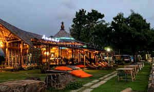 Avoin rakennus valaistuksella ja ulkotiloilla, nurmikon ja puiden ympäröimänä. (Tekoälyn luoma teksti)