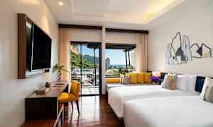 Hotellihuone, jossa kaksi valkoista sänkyä ja keltaisia tyynyjä, moderni sisustus ja parveke, jolta on näkymä vuorille ja merelle. (Tekoälyn luoma teksti)