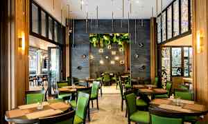 Ravintola, jossa pöytiä ja tuoleja, vihreitä yksityiskohtia ja koristeellisia seinäelementtejä. (Tekoälyn luoma teksti)