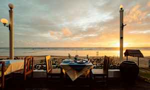 Näköala rannalle auringonlaskun aikaan, edessä katettu pöytä ja tuolit. (Tekoälyn luoma teksti)