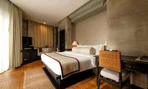 Hotellihuone, jossa on iso vuode pedattuna, kirjoituspöytä ja tuoli sekä televisio viihtyisässä ja valoisassa sisustuksessa. (Tekoälyn luoma teksti)