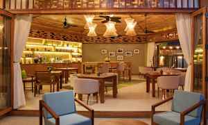 Ravintolan sisustus, jossa on kodikas tunnelma, puukalusteet, pöydät ja tuolit sekä koristeellisia lamppuja. (Tekoälyn luoma teksti)