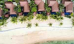 Ilmakuva rantamajoista, joita ympäröi kasvillisuus ja palmut. (Tekoälyn luoma teksti)