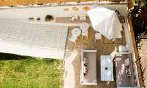 Näköala terassille, jossa on istuinryhmiä, pöytiä, aurinkovarjoja ja nurmikko. (Tekoälyn luoma teksti)