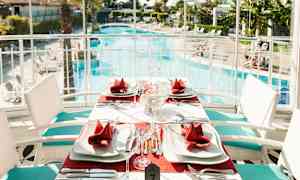 Pöytä, jossa punaiset servietit ja valkoiset lautaset, uima-altaan vieressä. (Tekoälyn luoma teksti)