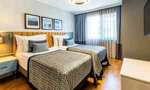 Hotellihuone, jossa on kaksi yhden hengen vuodetta, moderni sisustus ja luonnonvaloa ikkunasta. (Tekoälyn luoma teksti)