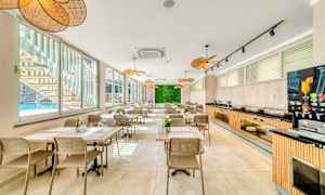 Nykyaikainen ja valoisa ruokailualue, jossa on useita pöytiä ja istumapaikkoja, isot ikkunat uima-altaan suuntaan ja viherseinä päädyssä. (Tekoälyn luoma teksti)