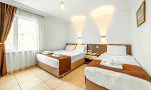 Hotellihuone, jossa on kaksi erillistä sänkyä, vaalea sisustus ja ikkuna, jossa on tummat verhot. (Tekoälyn luoma teksti)