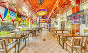 Ravintola, jossa puupöydät ja tuolit, sekä värikkäitä lippuja roikkuu katosta. (Tekoälyn luoma teksti)