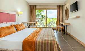 Hotellihuoneen sisätila, jossa on iso sänky, parveke ulkokalusteilla ja televisio seinällä. (Tekoälyn luoma teksti)