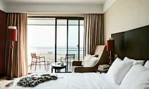 Hotellihuone, jossa on iso sänky, nojatuoli ja parveke merinäköalalla. (Tekoälyn luoma teksti)