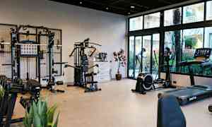 Kuntosali, jossa on erilaisia kuntoilulaitteita ja painoja sekä lasi-ikkunoita, jotka tarjoavat näkymän ulos. (Tekoälyn luoma teksti)
