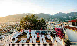 Terassi, jolla on aurinkotuoleja ja aurinkovarjoja, sekä näkymä kaupungin yli taustalla oleville vuorille. (Tekoälyn luoma teksti)