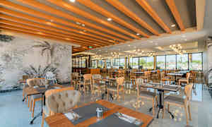 Moderni ravintola, jossa on suuret ikkunat, puuhuonekaluja ja koristeellisia kattoparruja. (Tekoälyn luoma teksti)