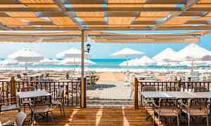 Ulkoterassi, jossa pöytiä, tuoleja ja aurinkovarjoja lähellä merta. (Tekoälyn luoma teksti)