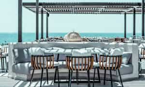 Ulkopöytä, jossa kori-tuolit ja pehmeät tyynyt, sijaitsee terassilla merinäköalalla. (Tekoälyn luoma teksti)