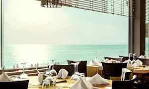 Ravintola, jossa katettuja pöytiä ikkunan edessä, josta näkyy meri. (Tekoälyn luoma teksti)