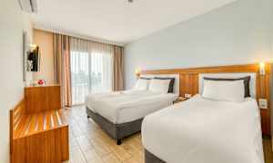 Moderni hotellihuone, jossa on kaksi sänkyä, vaaleat värit ja suuret ikkunat. (Tekoälyn luoma teksti)