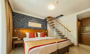 Hotellihuone, jossa kaksi sänkyä, koristeellinen tapetti ja kierreporras ylös. (Tekoälyn luoma teksti)