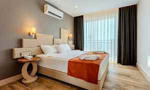 Hotellihuone, jossa on suuri sänky, yöpöytä ja ikkuna pimennysverhoilla. (Tekoälyn luoma teksti)