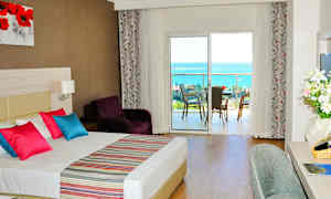 Hotellihuone, jossa parivuode, värikkäitä tyynyjä ja näkymä parvekkeelta merelle. (Tekoälyn luoma teksti)
