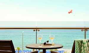 Parveke, jossa pöytä, kaksi lasia ja kirja merinäkymällä. (Tekoälyn luoma teksti)