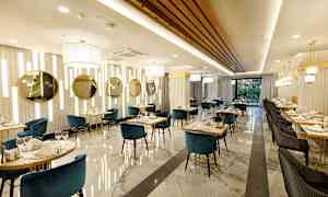 Kuvassa tyylikäs ravintola, jossa on sinisiä ja mustia tuoleja, marmorilattia ja kullanvärisiä yksityiskohtia. (Tekoälyn luoma teksti)