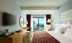 Moderni hotellihuone, jossa on sänky, kirjoituspöytä, nojatuoli ja parveke näkymällä. (Tekoälyn luoma teksti)