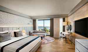 Hotellihuone, jossa suuri sänky, istuinalue ja parveke merinäköalalla. (Tekoälyn luoma teksti)