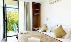 Hotellihuone, jossa on pedattu sänky, avoin kaappi ja parvekkeen ovi, joka johtaa ulkopatiolle. (Tekoälyn luoma teksti)