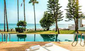 Rannalla sijaitseva uima-allas, aurinkotuoleja ja ympäröiviä palmuja. (Tekoälyn luoma teksti)