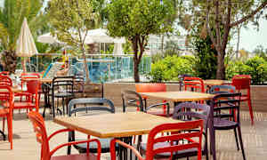 Värikkäitä tuoleja ja pöytiä ulkoterassilla vehreyden ja uima-altaan vieressä. (Tekoälyn luoma teksti)