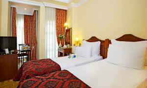 Hotellihuone, jossa kaksi erillissänkyä, punaisia koristeita ja verhot. (Tekoälyn luoma teksti)