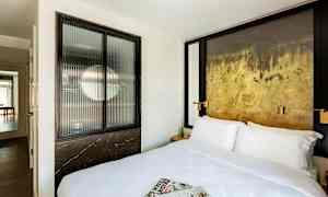 Hotellihuone, jossa on iso sänky, sanomalehtiä sängyllä ja koristeellinen seinä. (Tekoälyn luoma teksti)