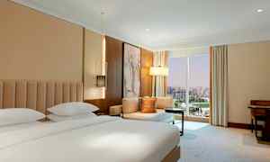 Hotellihuone, jossa on parivuode, istuinryhmä ja suuri ikkuna, josta on näkymät kaupunkiin. (Tekoälyn luoma teksti)