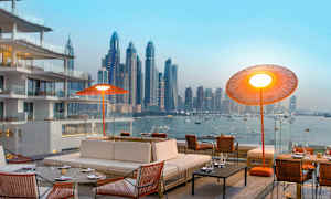 Moderni ulkoalue, jossa mukavat istuimet ja näkymä kaupungin siluettiin veden äärellä. (Tekoälyn luoma teksti)