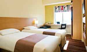 Hotellihuone, jossa on kaksi yhden hengen vuodetta, työpiste ikkunan ääressä ja modernit kalusteet. (Tekoälyn luoma teksti)