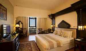 Hotellihuone, jossa on parisänky, kirjoituspöytä ja istuinalue. Ikkunassa on koristeellisia yksityiskohtia. (Tekoälyn luoma teksti)