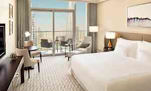 Moderni hotellihuone, jossa suuri sänky, istumaryhmä ja parveke, jolta on näkymä suurkaupunkiin. (Tekoälyn luoma teksti)