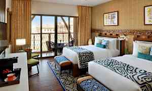 Kaksi pedattua sänkyä hotellihuoneessa, jossa on moderni sisustus, suuret ikkunat parvekkeelle ja näkymä. (Tekoälyn luoma teksti)