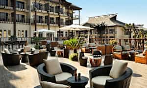 Ulkoterassi, jossa modernit istuimet, aurinkovarjot ja kasveja, rakennusten ympäröimänä. (Tekoälyn luoma teksti)