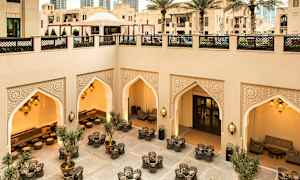 Taidokkaasti suunniteltu sisäpiha, jossa istumaryhmiä, itämaisia koristellisia holveja ja valaistus; ympäröivät moderni ja perinteinen arkkitehtuuri. (Tekoälyn luoma teksti)