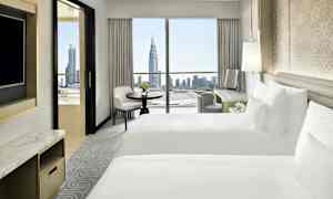 Hotellihuone, jossa on kaksi valkoista sänkyä, työpöytä ja ikkuna näkymällä kaupunkiin pilvenpiirtäjineen. (Tekoälyn luoma teksti)